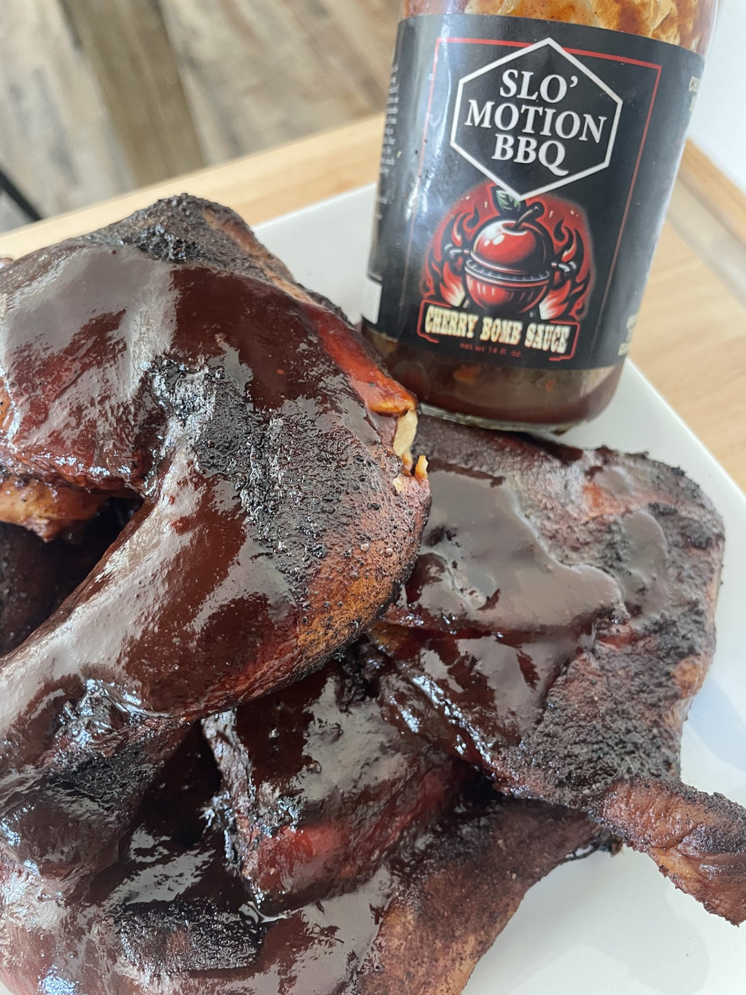 Barbecued meat with a bottle of Slo' Motion BBQ Cherry Bomb Sauce on a white plate.