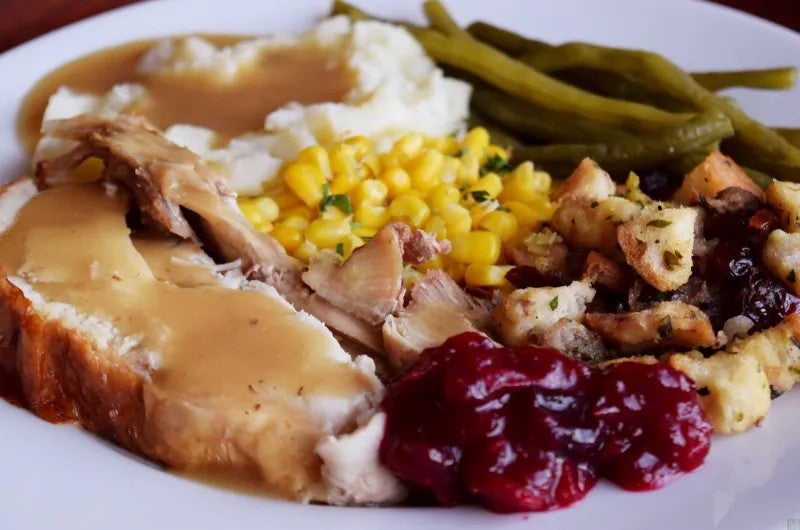 Plated meal with turkey, mashed potatoes, corn, green beans, and cranberry sauce on a white plate.